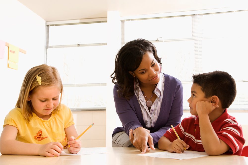 A woman is helping two children with writing.