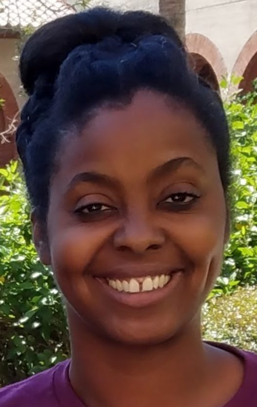 A woman smiling for the camera with trees in the background.